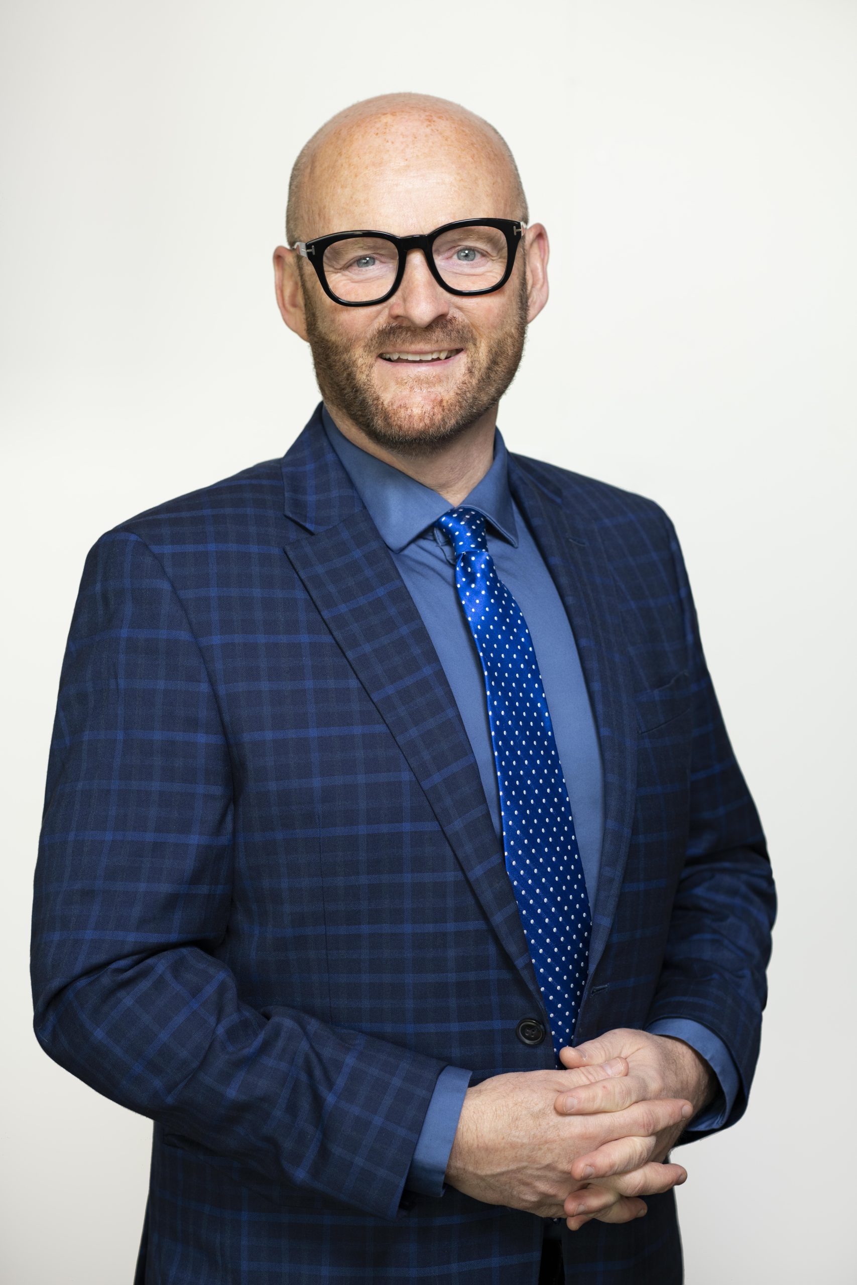 Portrait of auditor general Michael A. Pickup, wearing a blue checked blazer and blue tie with white polka dots