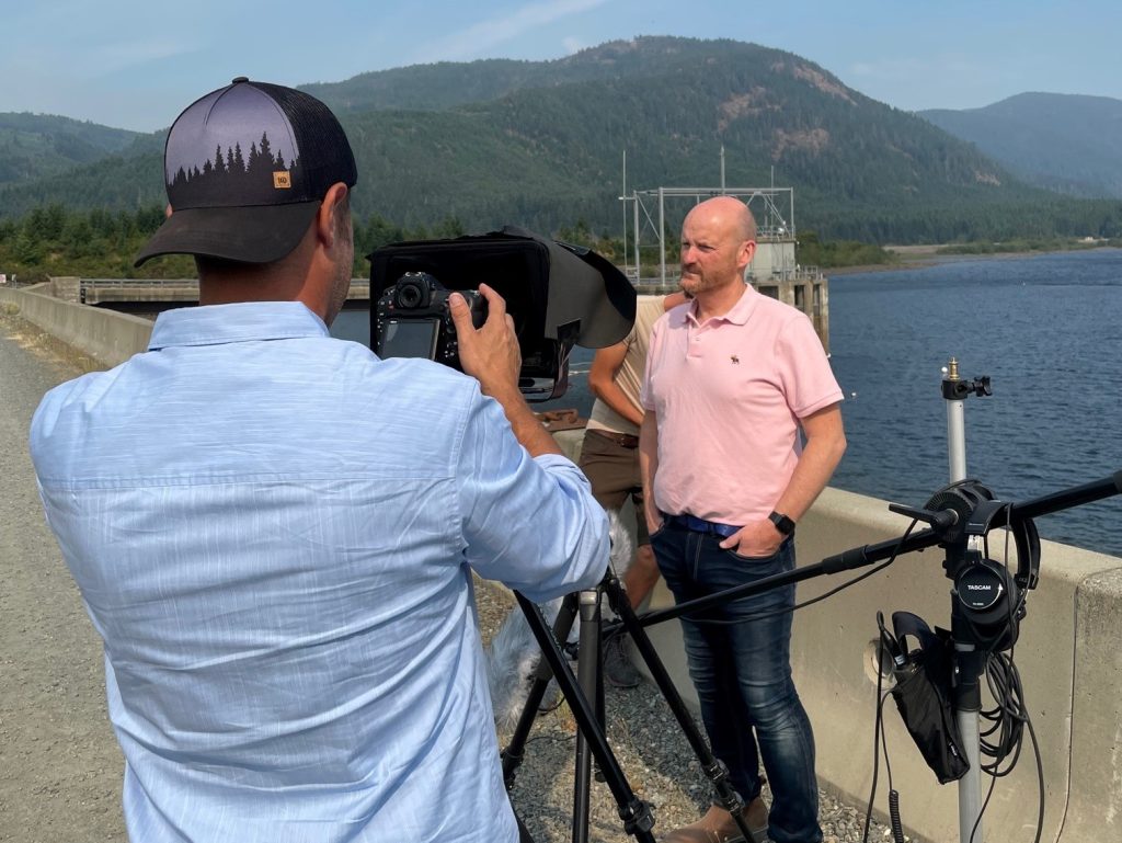 Auditor General Michael Pickup standing in front of the Sooke Reservoir while a staff prepares to video tape his presentation