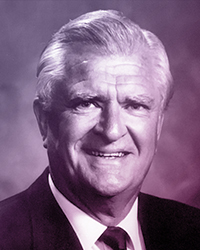 Portrait of an older man, short, slicked back white hair, in a suit and tie. Name: Robert Hayward.