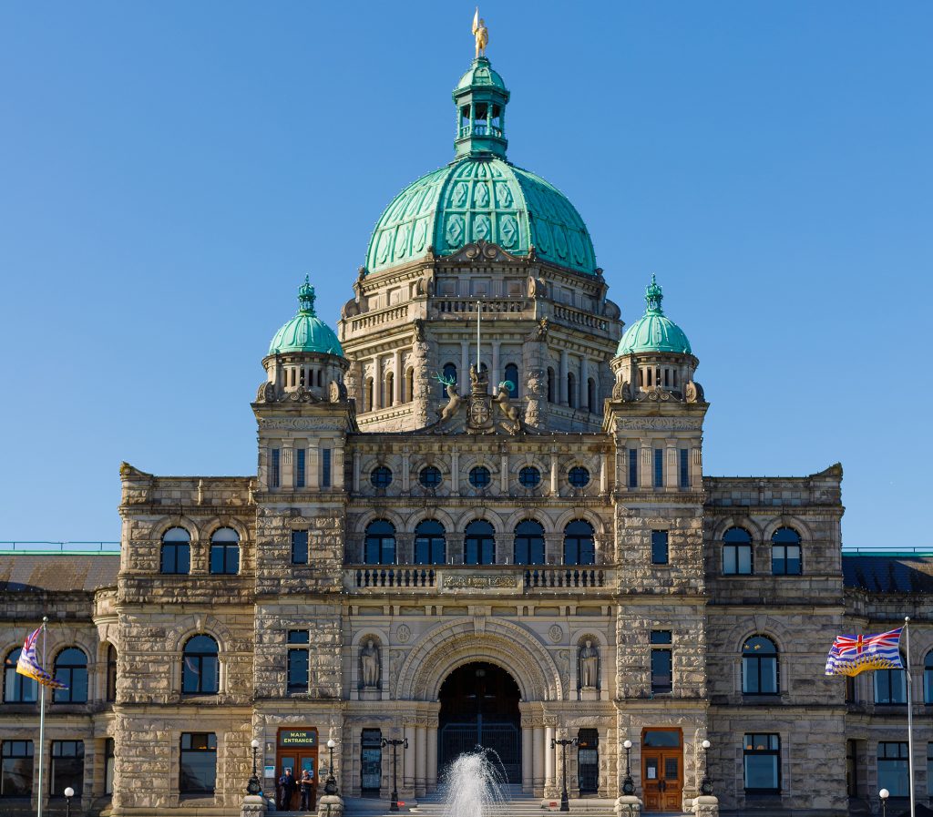 Front of British Columbia Parliament Buildings with fountain and flags.